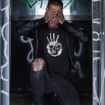 Man sieht einen Mann, der ein Zorn des Thrash - Herrenhemd trägt und sein Gesicht mit den Händen bedeckt.